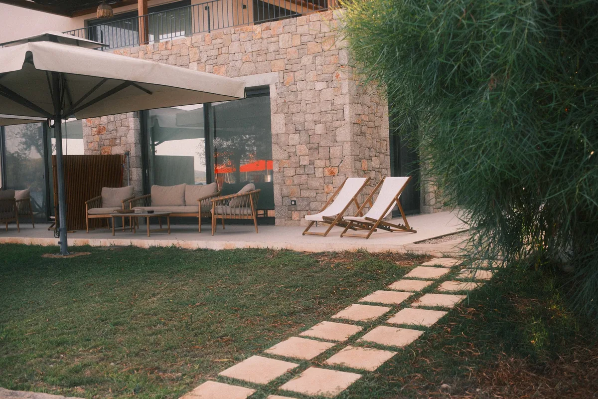 A wide stone terrace furnished for outdoor dining beside planting